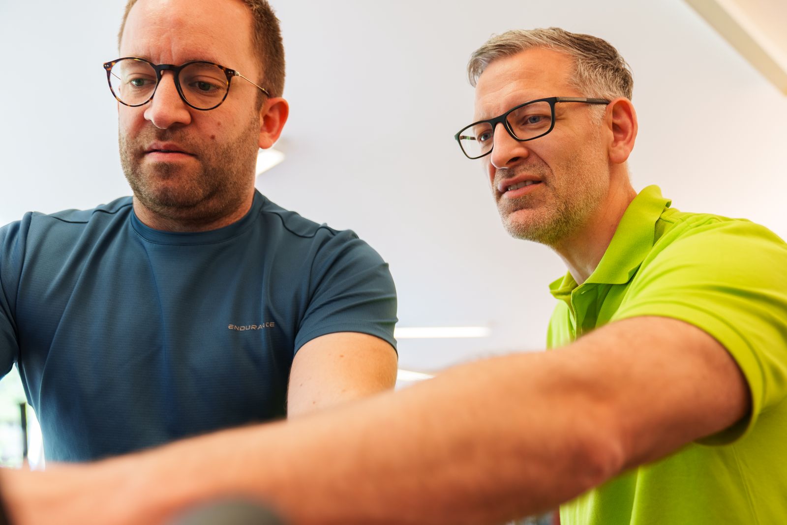 Therapeut des Therapie- & Gesundheitszentrums Dentl erklärt einem Patienten die Einstellung am Trainingsgerät